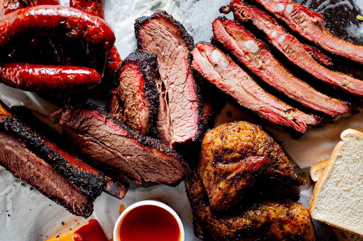 Close-up of slices of still-pink BBQ next to dipping sauces