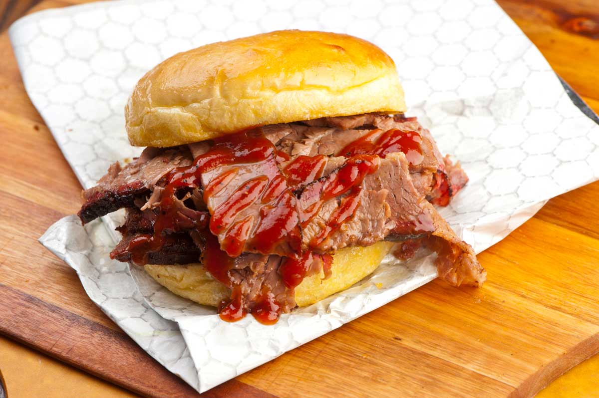 A brisket sandwich in wax paper slathered with BBQ sauce