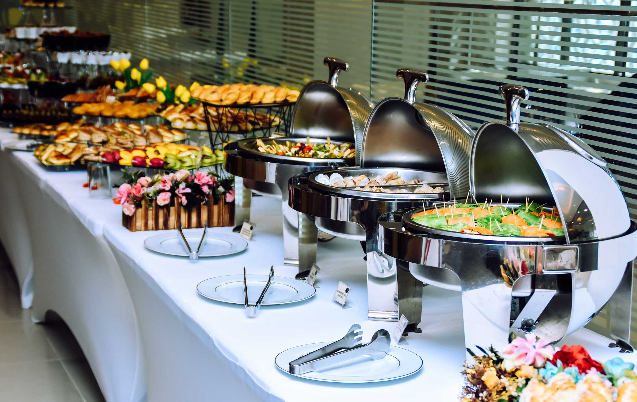 A long buffet table covered with various trays of fruits, meats, kebabs, and other foods