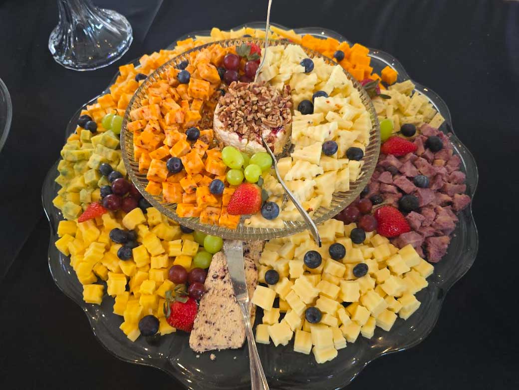 A round, two-layer catering dish covered with cubes of cheese and meat speckled with blueberries