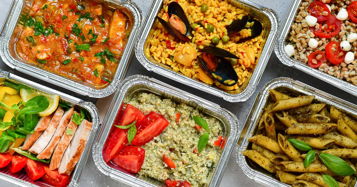 Several square foil serving trays filled with different foods like rice, clams, and pasta