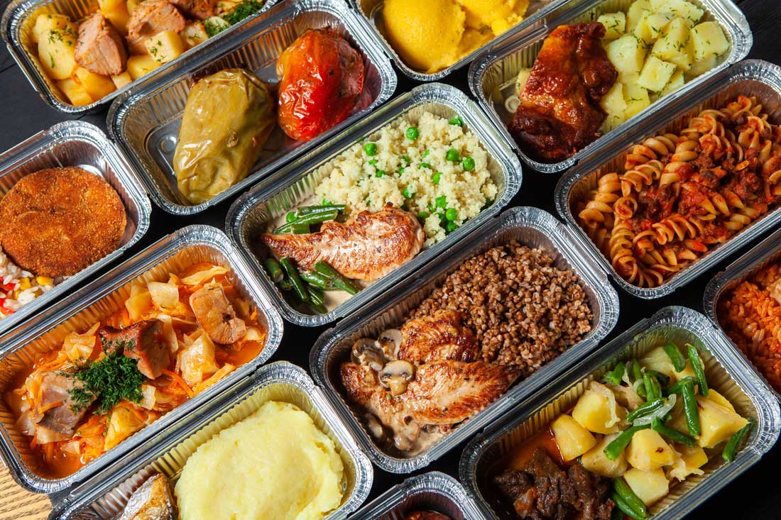 Rows of foil trays filled with various catering meals with rice, meats, and potatoes