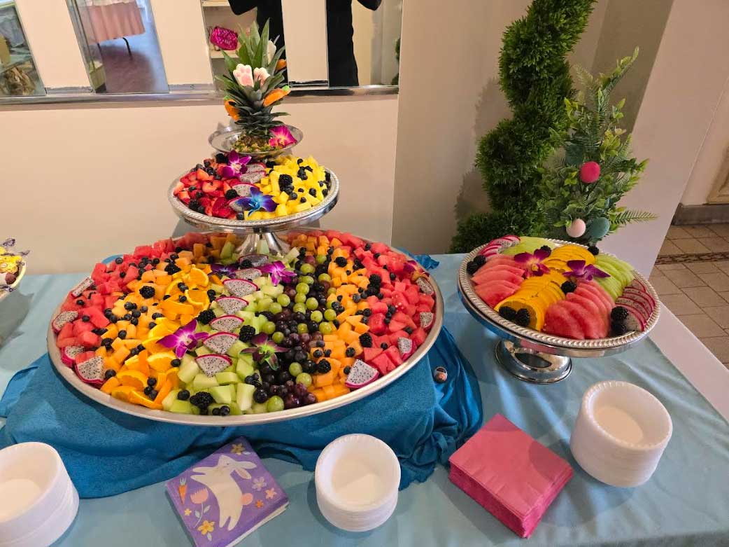 One large and one smaller serving tray on a banquet table covered in rows of different fruit