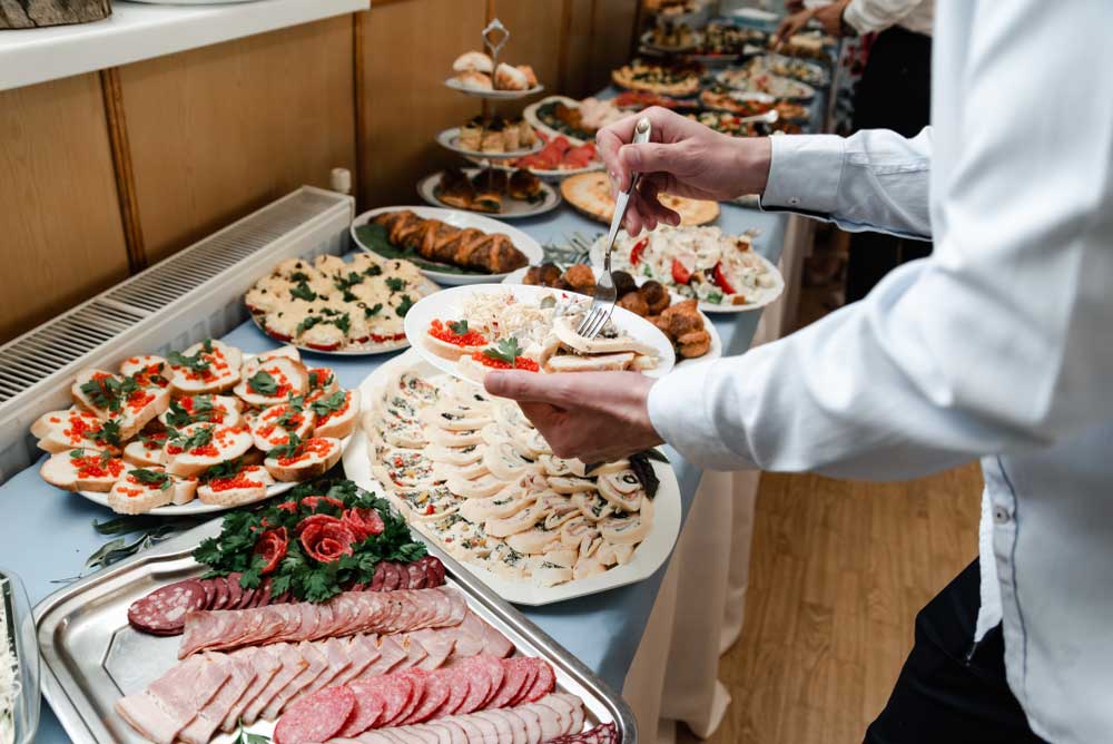 A guest getting slices of turkey from a buffet table that's covered with platters of meat, cheese, fruit, and other foods