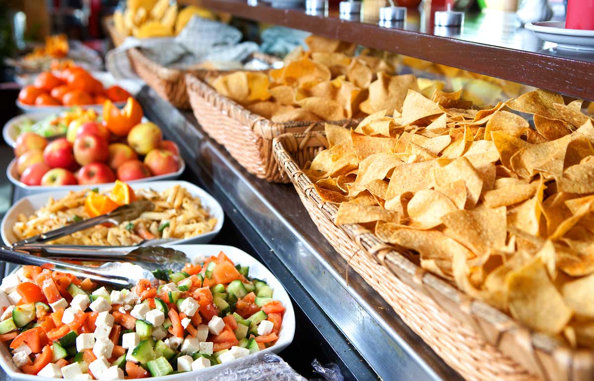 A mexican buffet table covered with baskets of chips and platters of vegetables and pasta