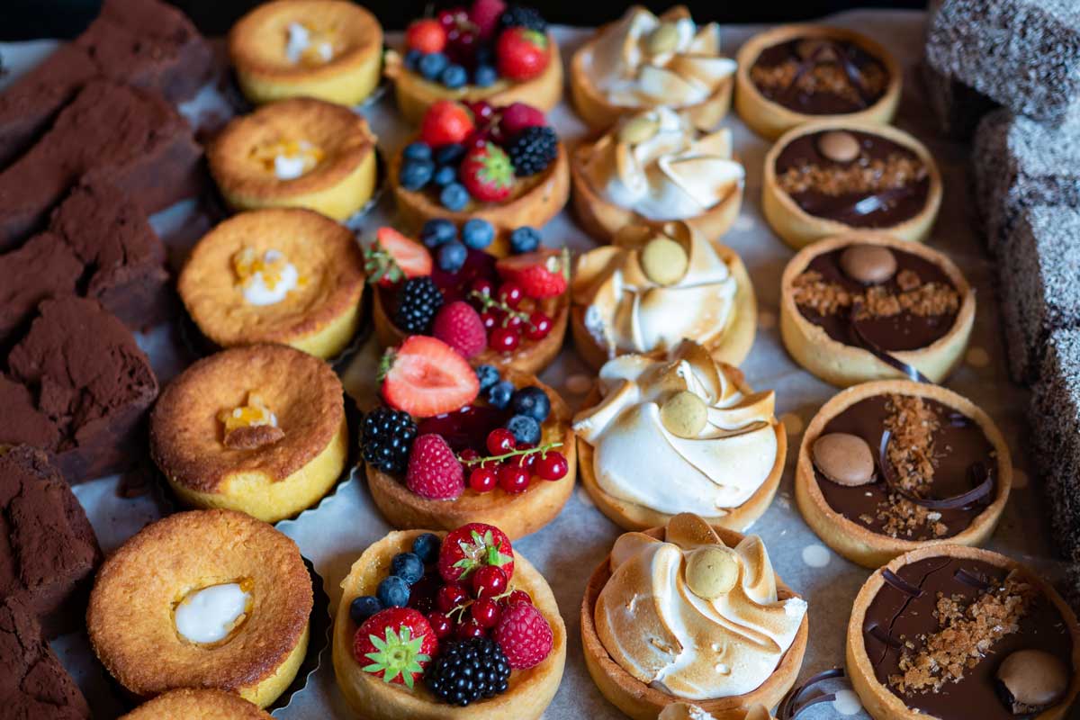 Rows of delicately prepared pastries, some covered with fruit, others covered with chocolate