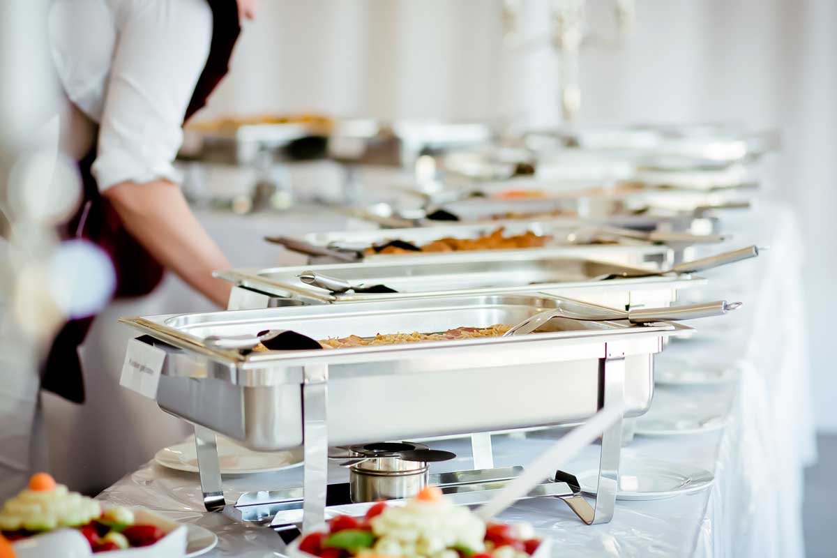 A long table covered in warming trays filled with food