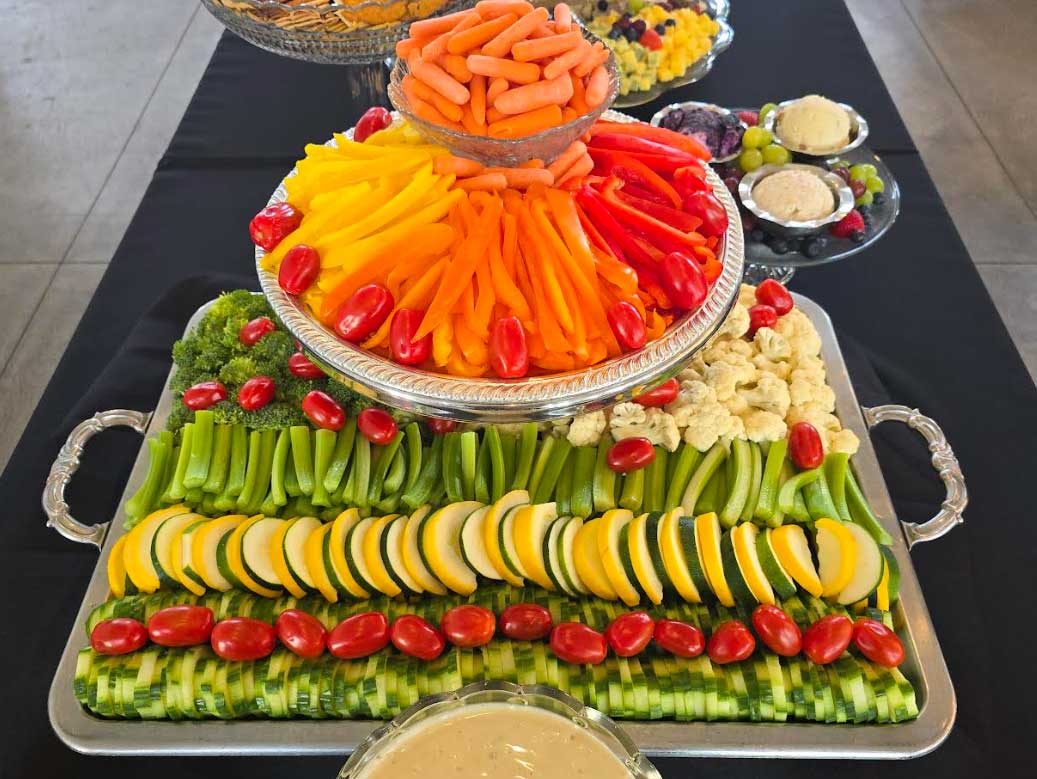 A large tray of vegetables neatly organized on a banquet table