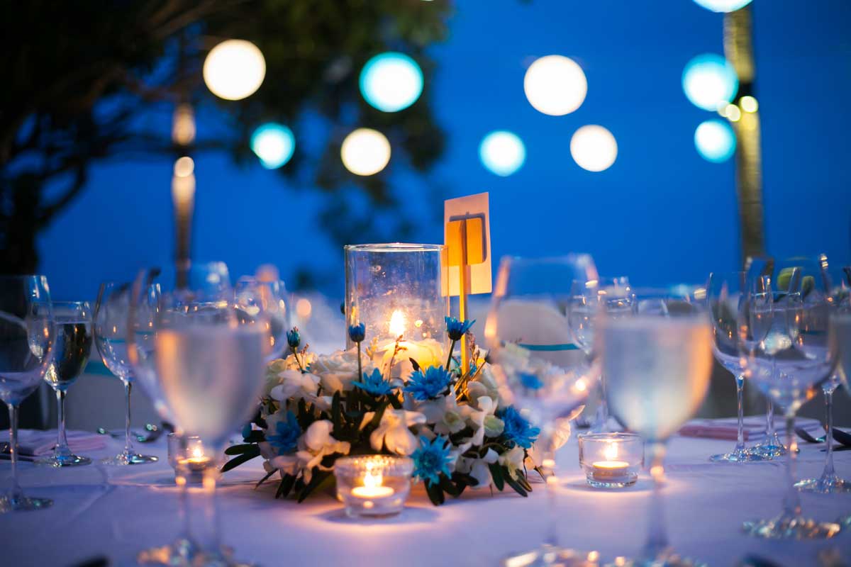 A table at an outdoor wedding venue covered with drinking glasses, candles, and flowers